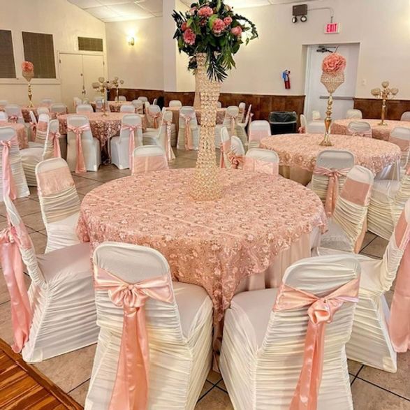 Elegant event space with round tables draped in pink lace, decorated with floral centerpieces.