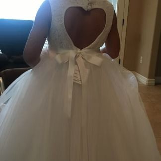 Girl in white dress with heart-shaped open back, light tulle skirt, and ribbon closure.