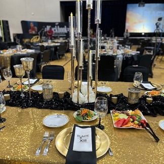 Formal dining table setting with gold sequin tablecloth, black runners, and tall candle holders.
