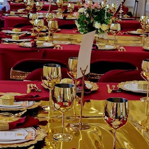 Tables set for a formal event with red tablecloths, gold accents, and wine glasses, a floral centerpiece.
