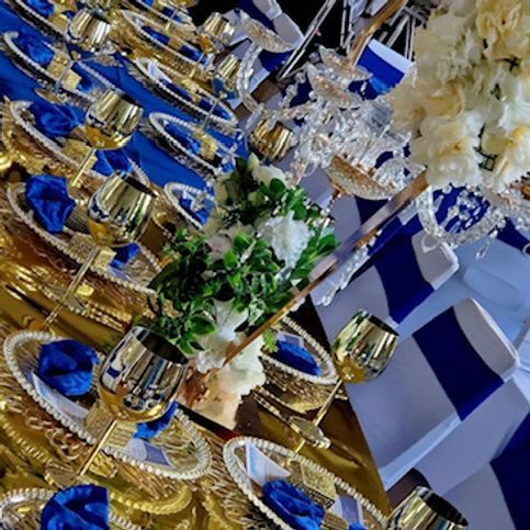 Elegant table setting with gold accents, blue napkins, white flowers, and decorative flags.