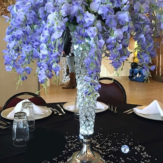 Centerpiece with lavender flowers cascading from a crystal-studded vase on a black tablecloth.