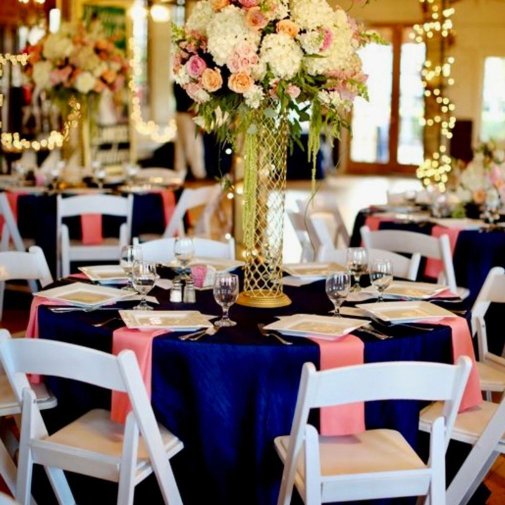 Wedding reception tables with navy blue tablecloths, peach runners, and white chairs, topped with floral centerpieces.