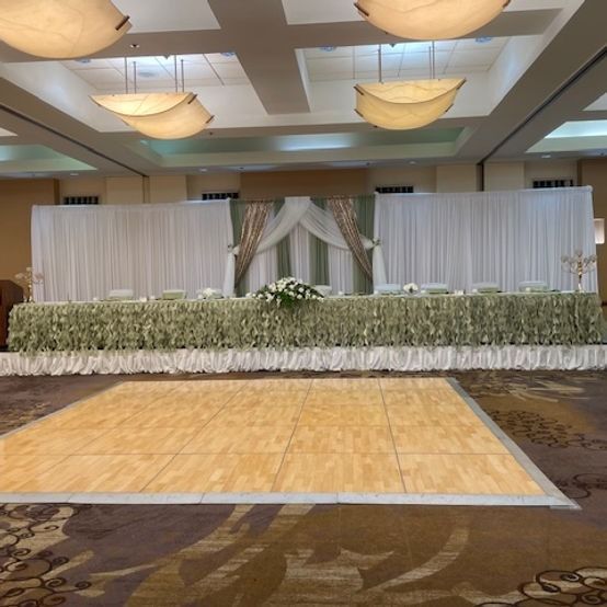 A decorated wedding reception hall with a dance floor. White and green accents on a long table.