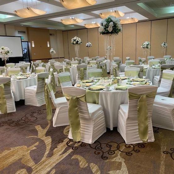 A banquet hall set for an event, with white tablecloths, chairs with green sashes, and floral centerpieces.