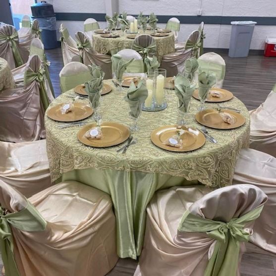 Round tables set for an event with gold and green tablecloths, napkins, and chair covers.