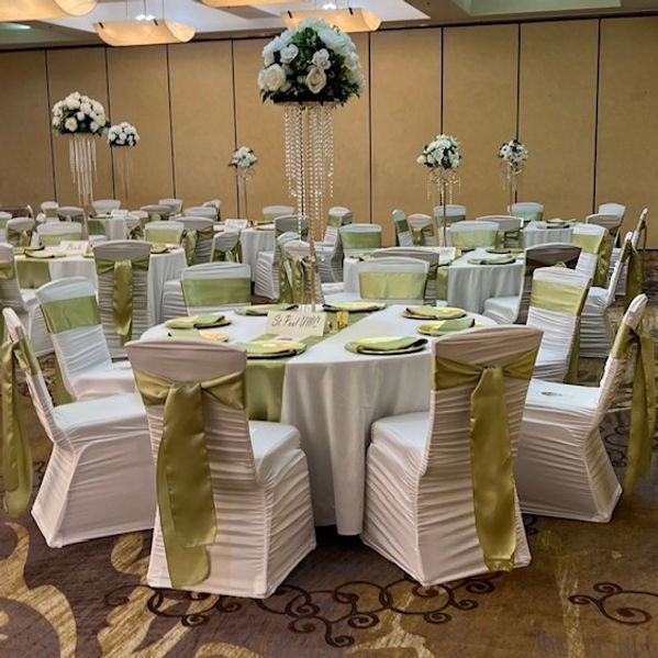 Banquet hall with round tables set for a formal event; white linens, gold accents, floral centerpieces.