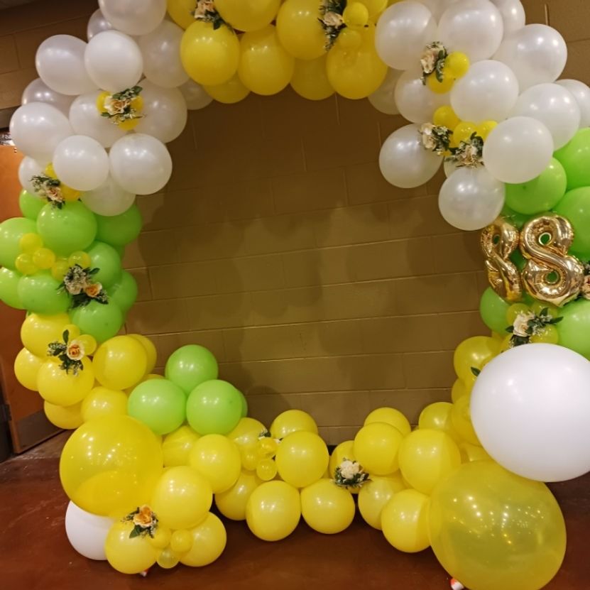 A circular balloon arch in yellow, white, and green, for a birthday celebration.