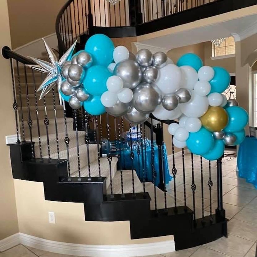 Balloon arch in turquoise, silver, white, and gold decorates a staircase for a party.