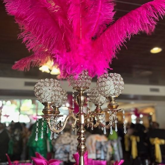 Bright pink feather centerpiece atop a gold candelabra with crystal accents, indoors at an event.
