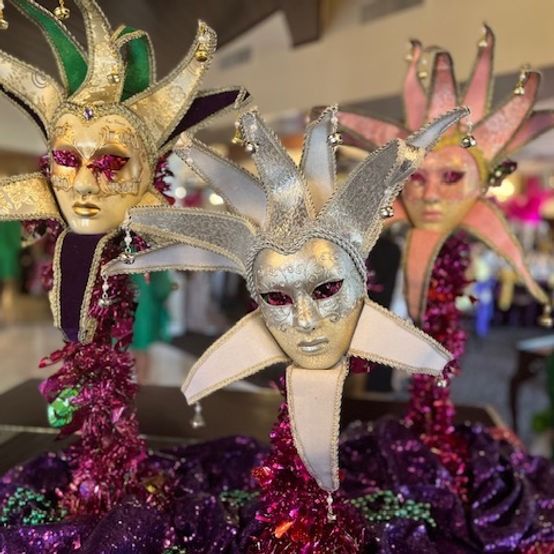 Three ornate Venetian masks with jeweled accents atop a shimmering purple and pink surface.