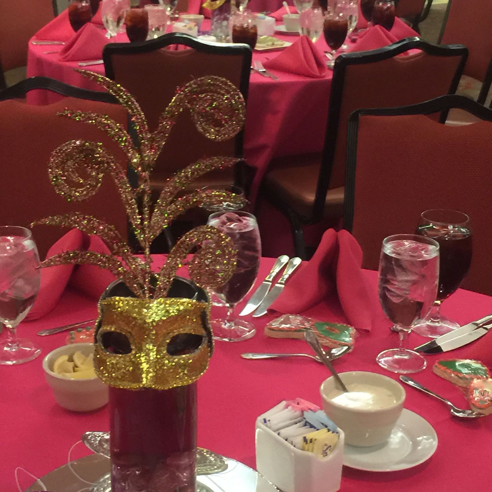 Mardi Gras themed table setting with mask centerpiece, pink tablecloth, and glasses.