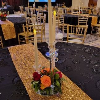 Elegant table setting: Black tablecloth, gold runner, floral centerpiece, candles.