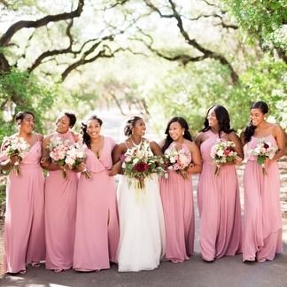 Bride and bridesmaids in pink dresses, holding bouquets, posing outdoors.