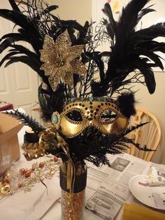 Gold and black Mardi Gras centerpiece with mask, feathers, and decorative floral elements.