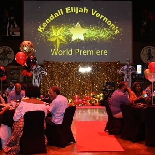 People at a world premiere event. Gold and red decor, balloons, projector screen with a star logo.