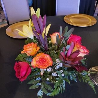 Centerpiece of orange, red, and purple flowers with golden charger plates on a black tablecloth.