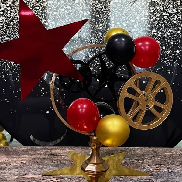 A Hollywood-themed centerpiece with balloons, star, and film reels, on a stage with a starry background.