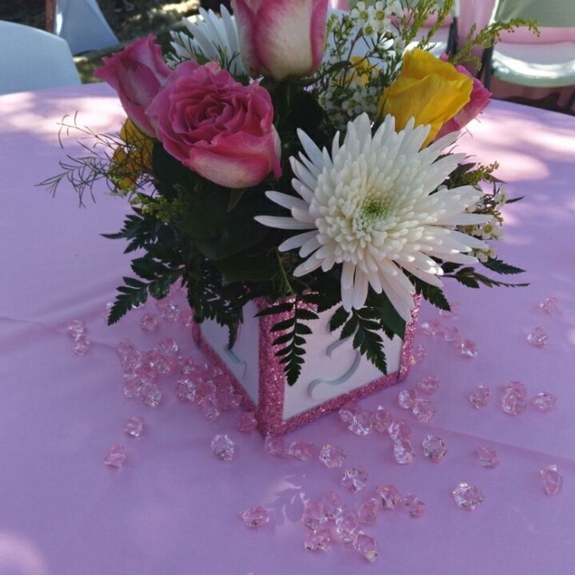Flower arrangement in pink-glitter-edged box with pink gems on a pink tablecloth; roses, daisies, and ferns.