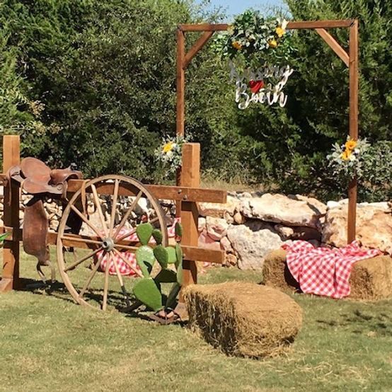 Western-themed outdoor scene: wooden arch with floral accents, hay bales, a saddle, and a wagon wheel.