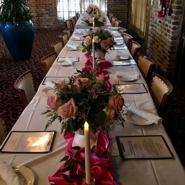 Long dining table set for a formal event with pink flower arrangements and candles.