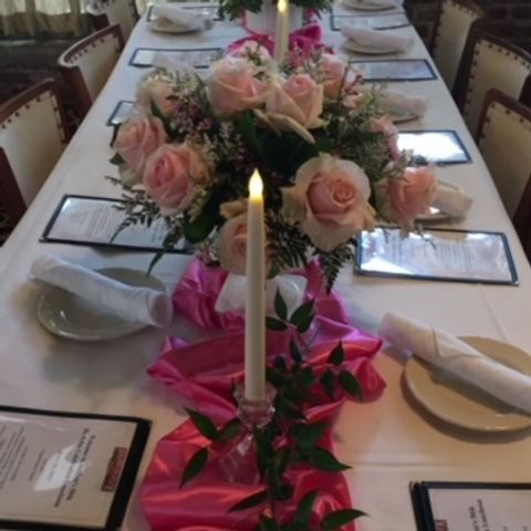 Formal dining table with pink roses, candle, and place settings.