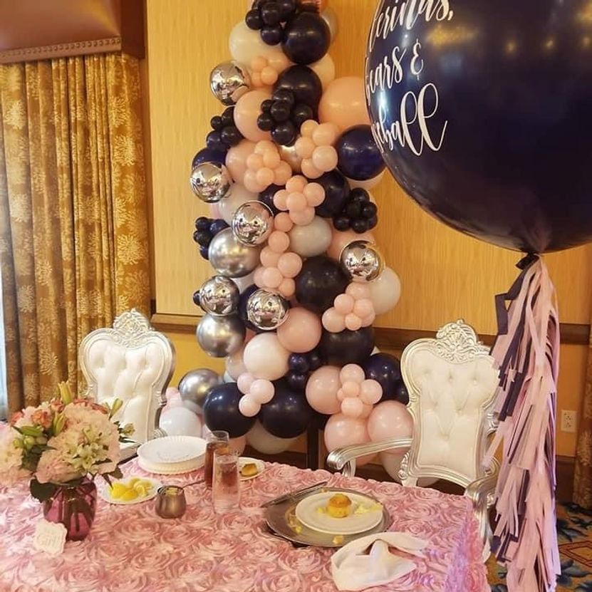 Party table with pink tablecloth, floral centerpiece, balloon arch, and large navy balloon.