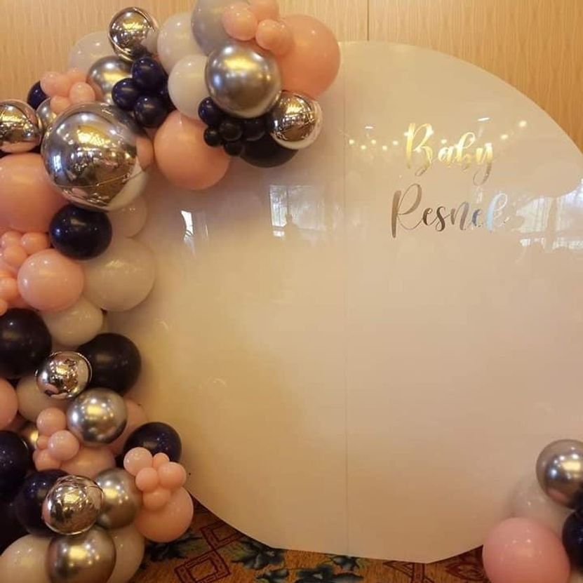 White circular backdrop with balloons in pink, navy, and silver, celebrating a baby shower.