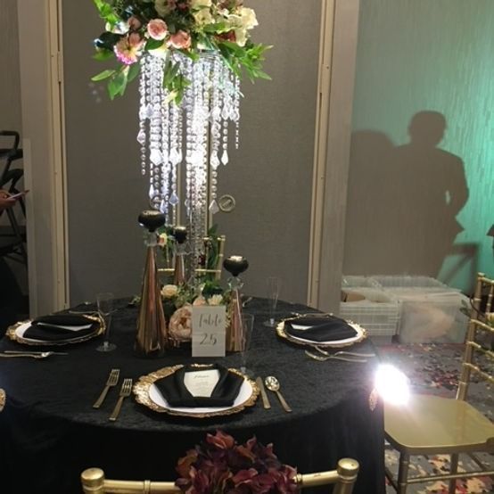 Elegant table setting with floral chandelier centerpiece, black tablecloth, gold accents.