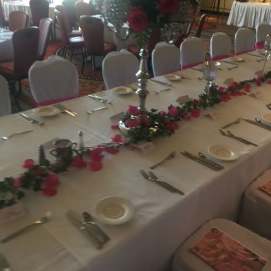 A long dining table set for a formal event, white tablecloth, roses, and silverware.