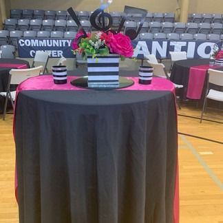 Round table set for an event, black tablecloth with a pink runner and centerpieces.