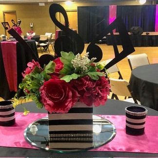 Centerpiece with red flowers, black & white striped vase, music notes, and pink accents at a table.