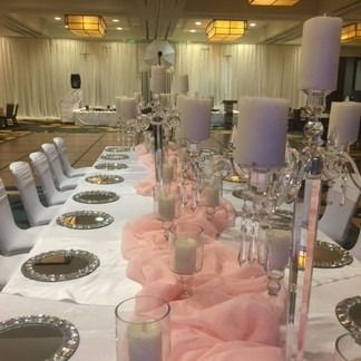 Long table set for a formal event; white linens, candelabras, candles, pink fabric runner, and mirrored chargers.