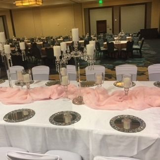 Formal dining table set for event with candelabras, pink runner, white tablecloth, and mirrored chargers.