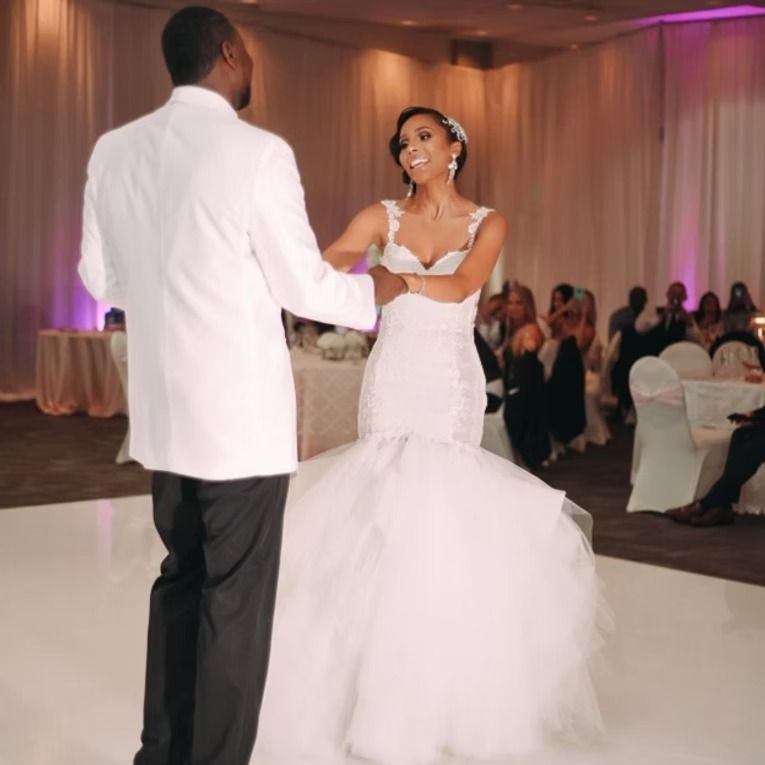 Bride and groom dancing at a wedding reception. Bride in white gown, groom in suit, smile.