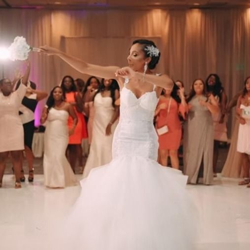 Bride tossing her bouquet at a wedding reception. White dress, smiles, indoors.