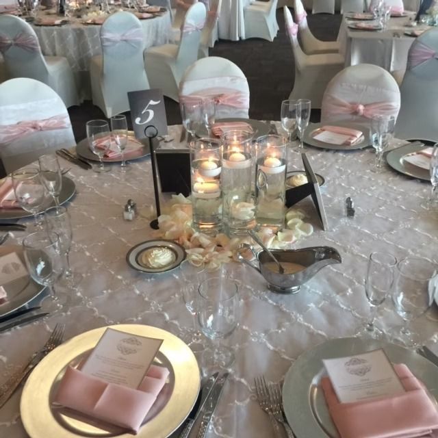 Wedding reception table set with silver chargers, pink napkins, and floating candles.