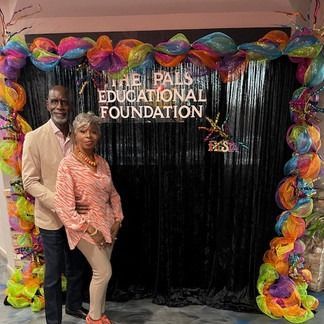 Couple poses in front of a black backdrop with colorful decorations for The Pals Educational Foundation.
