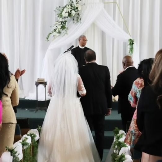 Bride walks down the aisle in a church towards a waiting officiant.