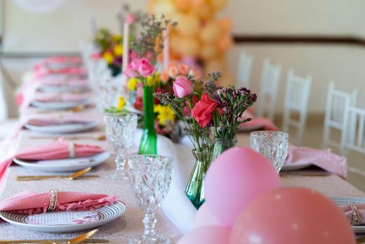 A decorated table set for a party with floral arrangements, pink and gold accents, and balloons.