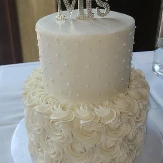 Two-tiered wedding cake with rosettes on the bottom tier, dots on the top tier, and a