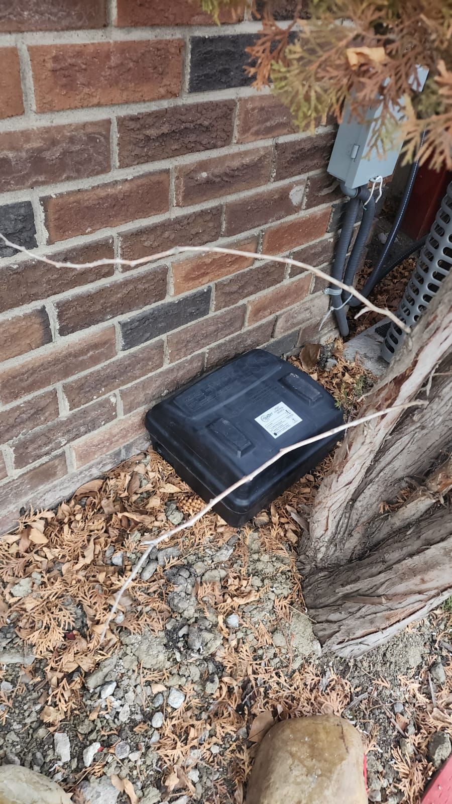 A black box is sitting on the ground next to a brick wall.