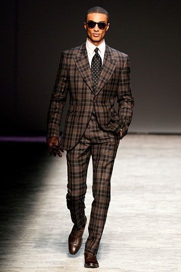a man is walking down a runway wearing a plaid suit and tie .