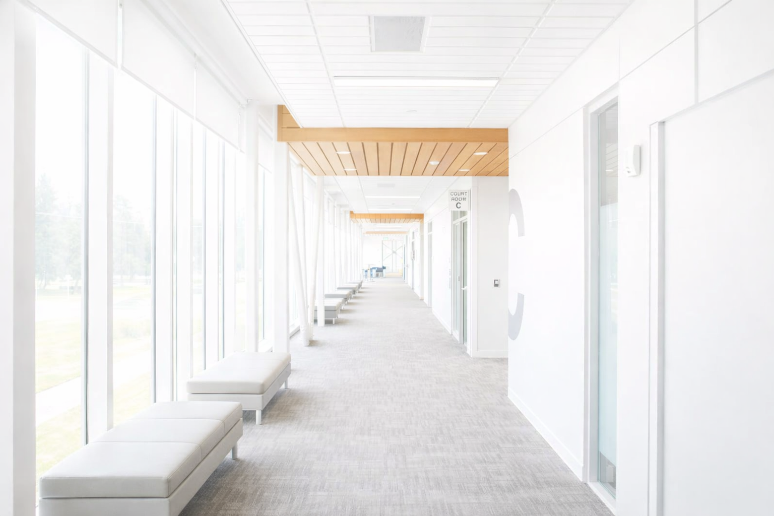 Bright, white hallway with large windows, benches, and a wooden ceiling.