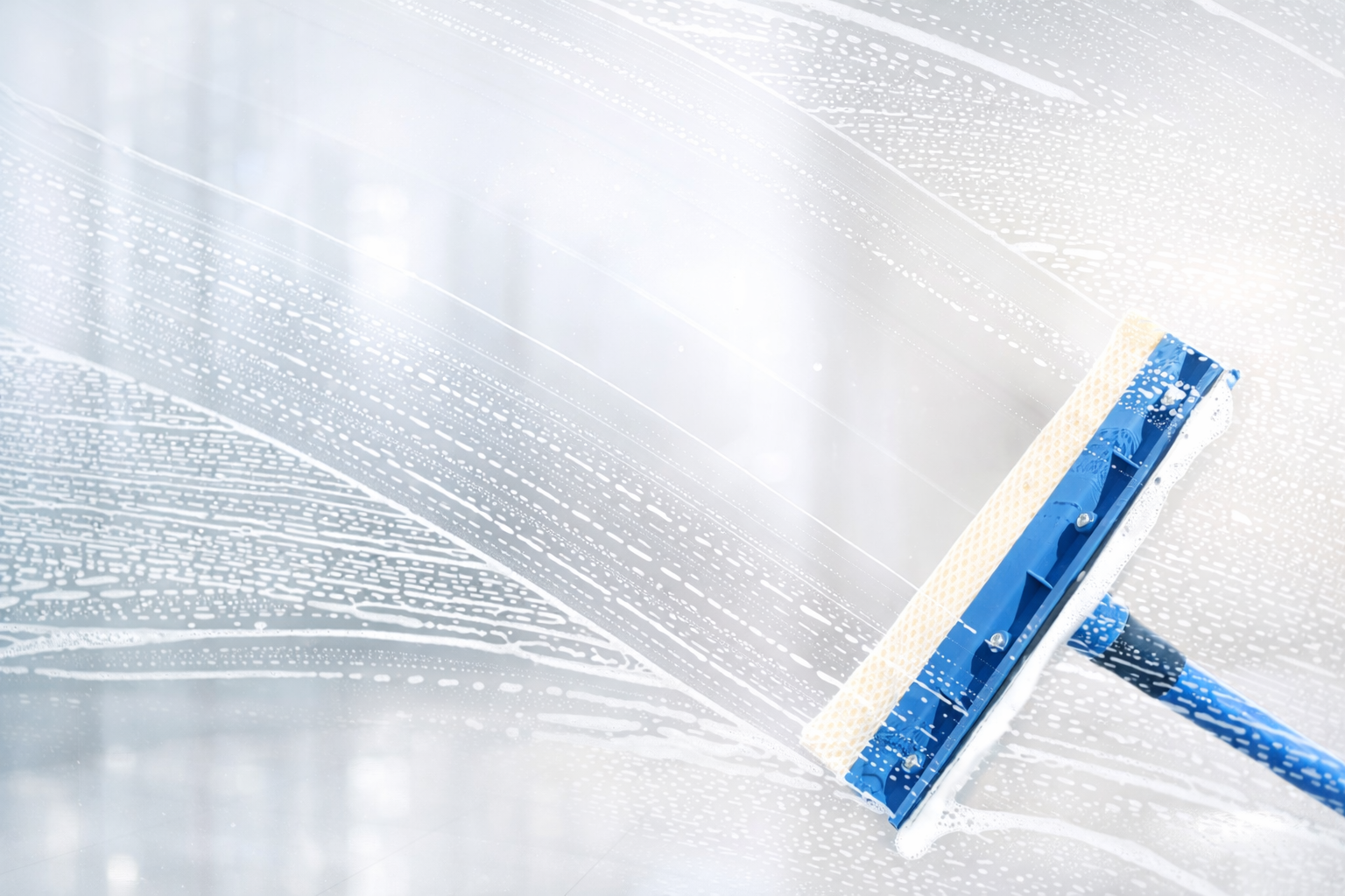 Blue and white squeegee cleaning a soapy window.