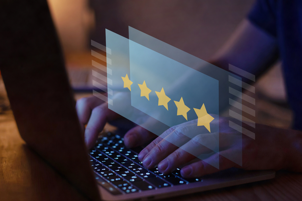 Person typing on laptop with overlay of five gold stars, suggesting positive online review.