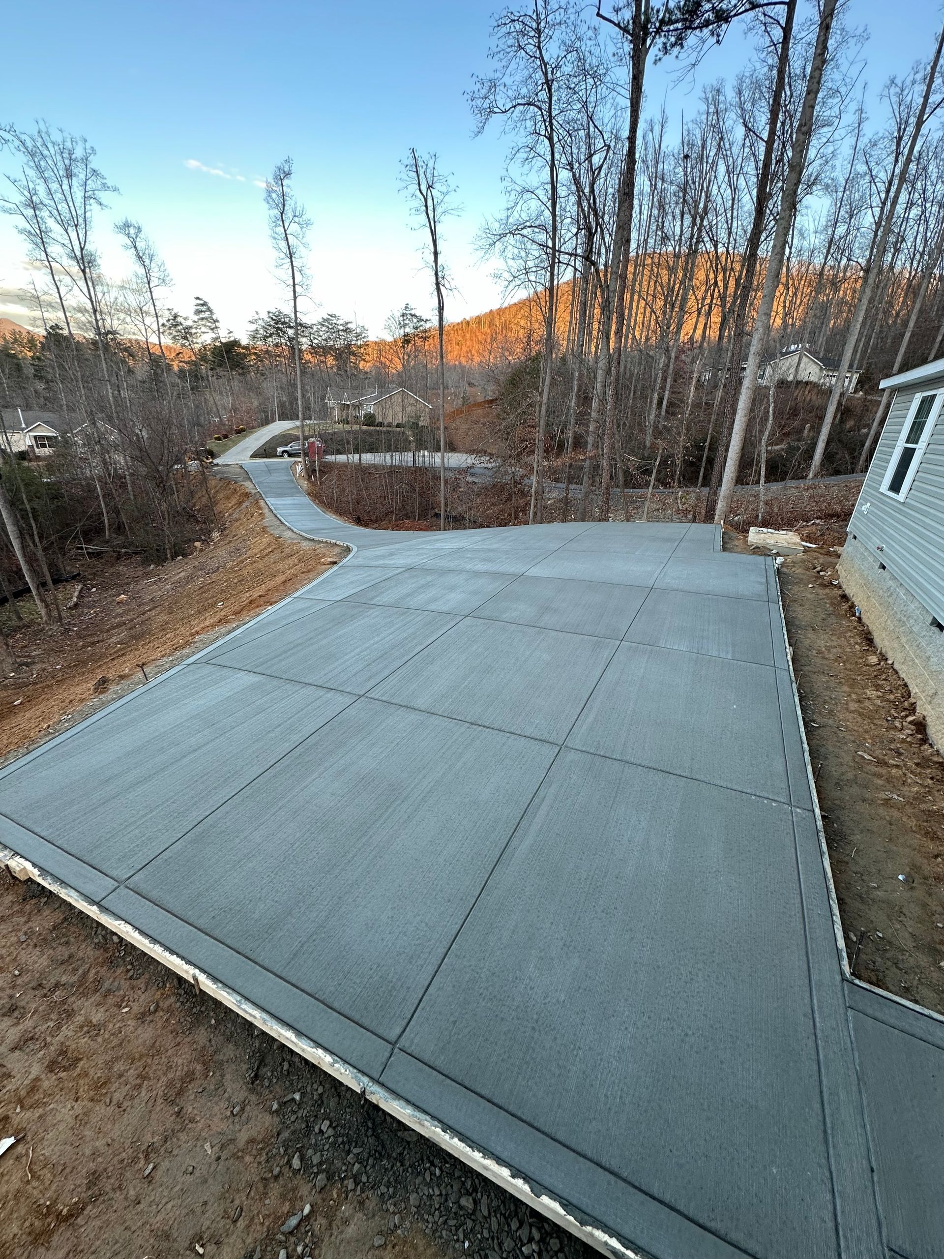 A freshly poured gray concrete patio with control joints leading to a sidewalk in a wooded yard.