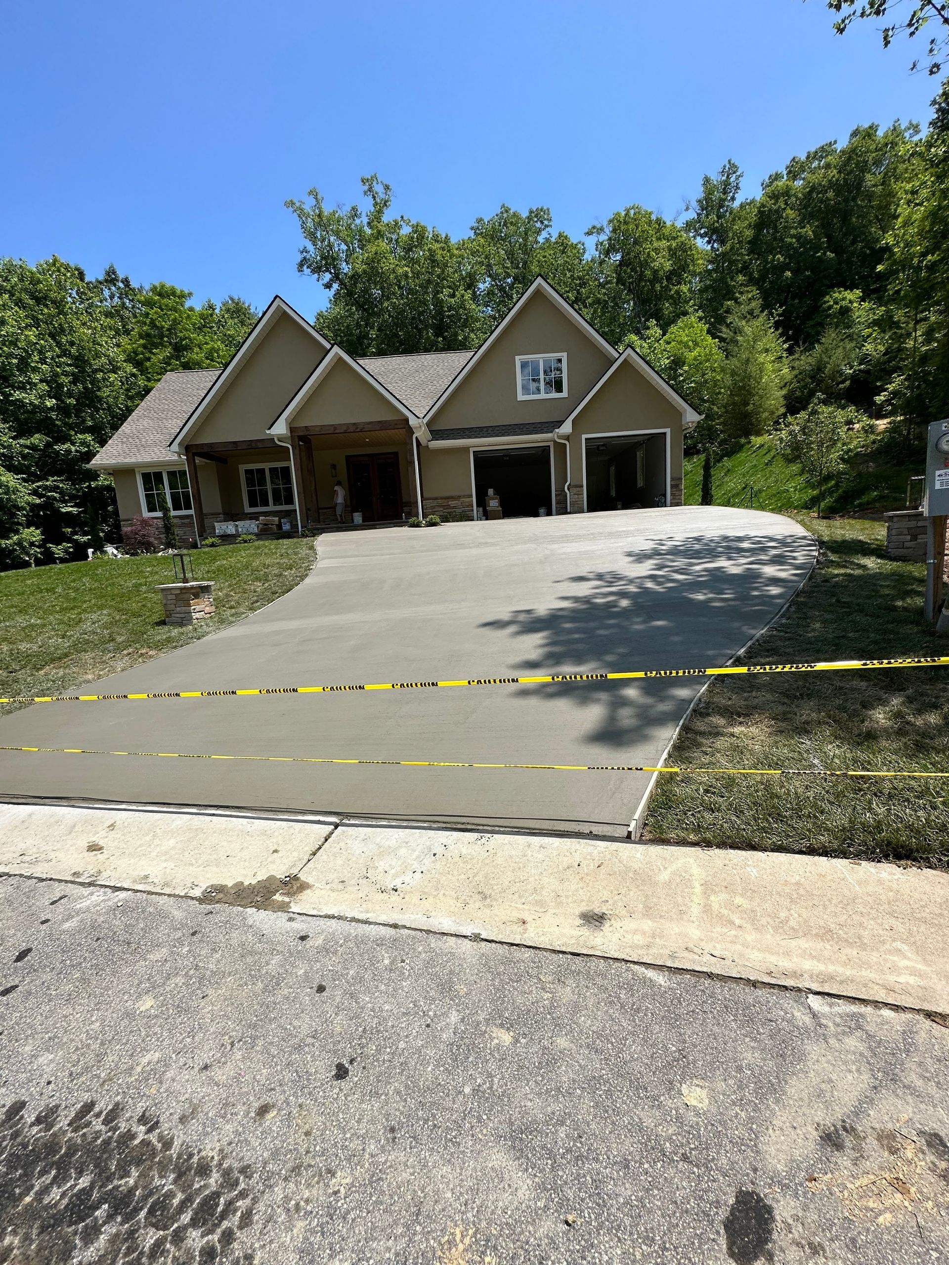 A tan house with a newly poured concrete driveway blocked off by yellow caution tape on a sunny day.