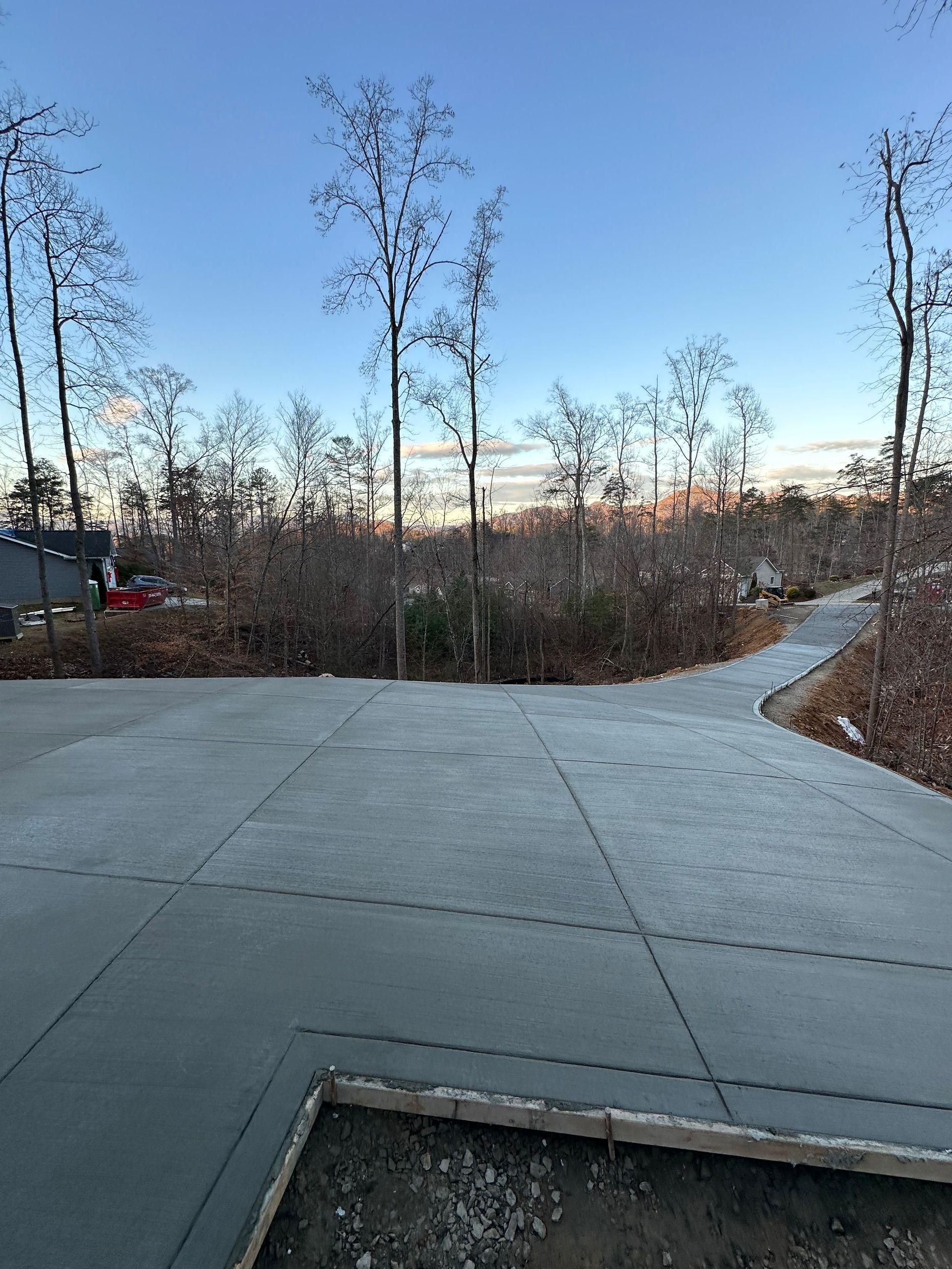Newly poured concrete driveway and walkway extending toward a wooded area under a clear blue sky.