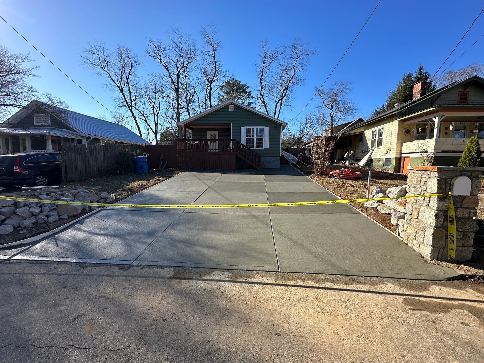 A residential street scene featuring a newly poured concrete driveway blocked by yellow caution tape.